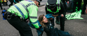 Two policeman try to lift a XR Scotland protester off the street