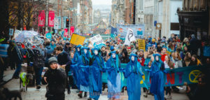 Blue figures leading a procession of protesters