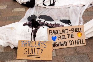 Climate activists shrouded as 'Dead bodies' covered in oil outside a Barcalays bank, Glasgow. Signs say 'Barclays Guilty' and 'Barclays + 'Shell fuel the highway to hell'.