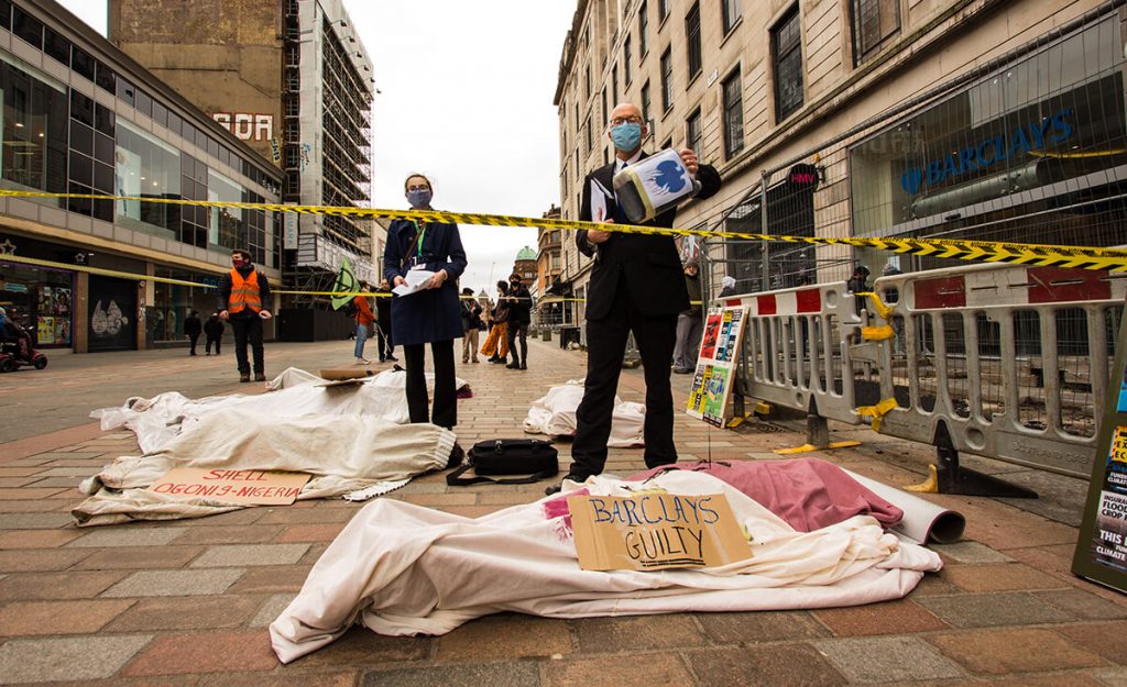 Climate activists stage performance outside a Barcalays bank, Glasgow using 'dead bodies' covered in oil. Sign say 'Barclays Guilty'.