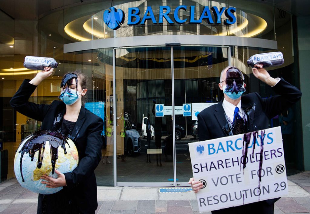 Climate activists in suits pour oil over themselves outside a Barcalays bank