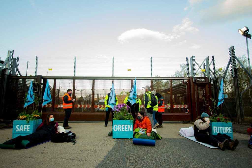 Three Extinction Rebellion Scotland activists locked to flower planters saying Safe, Green Future on them. Actvisists are in front of main gate to Faslane.