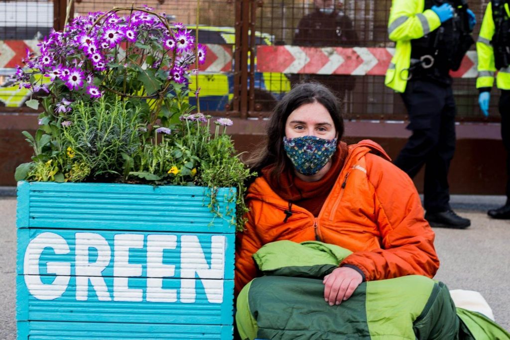 Activist locked to flower planter with 'Green' painted on it.