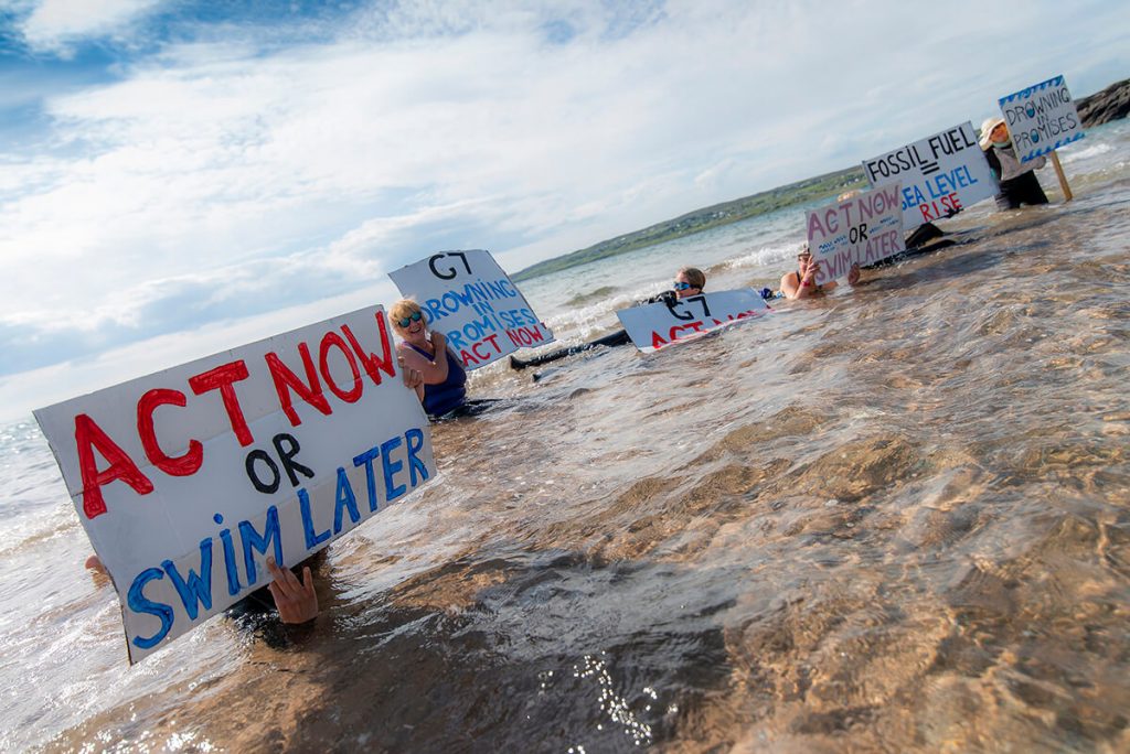 Climate activists pose in sea with placards saying 'Act now or Swim later' and 'G7: Drowing in promises - Act Now'