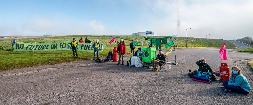 Peterhead Power Station: activists block road with banners, gas canisters and washing machine. Peterhead Power Station chimney in background shrouded by fog.