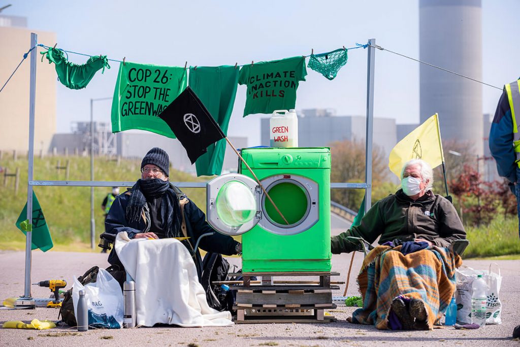 Activists sitting and locked onto green washing machine with Peterhead Power Station in background.