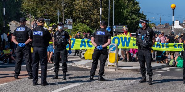 Protestors behind a line of police block a road at G7