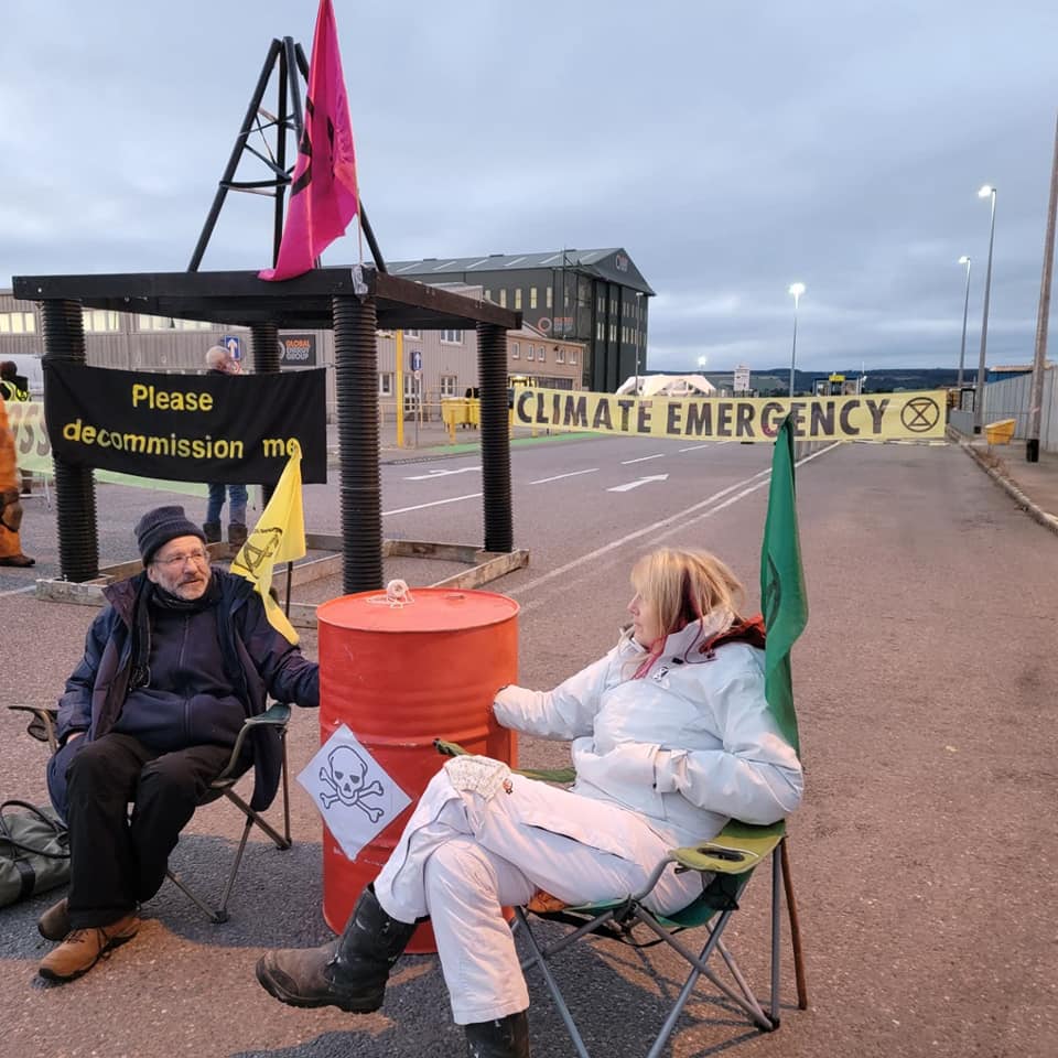 Two activists locked to oil barrel in front of model oil rig saying 'Decommission Me' on it