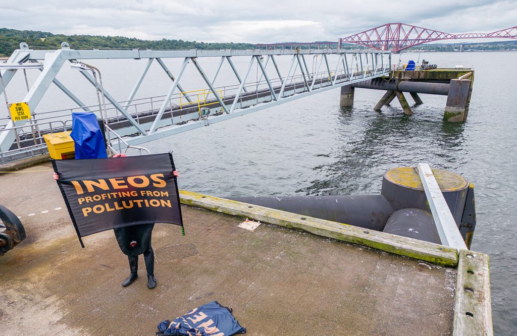 Protestor on oil terminal holding up banner that says 'Ineos: Profiting from Pollution'