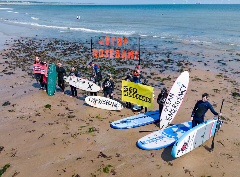 Kayakers and surfers on beachwith Stop Rosebank banners and boards