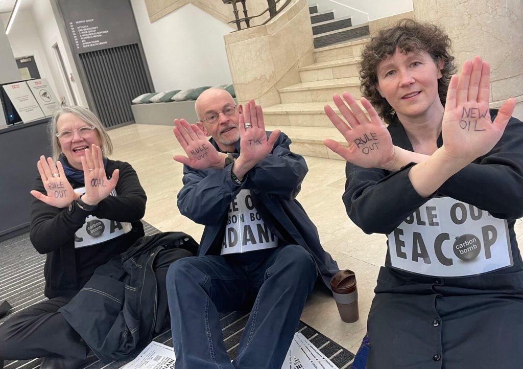 XR Scotland activists sit on floor occupying insurance company AIG office and hold up hands to the camera with Ruel out Coal, Rule out TMX and Rule out New Oil written on them