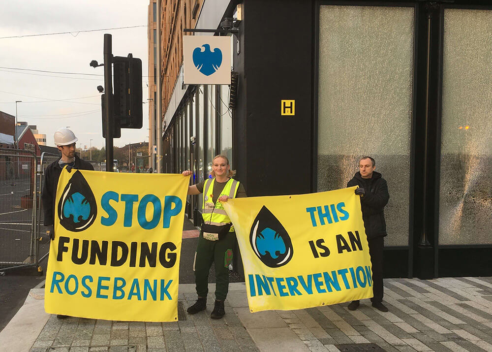 Activists stand outside Barclays branch with windows broken. They hold banners saying Stop Funding Rosebank and This is an Intervetion.