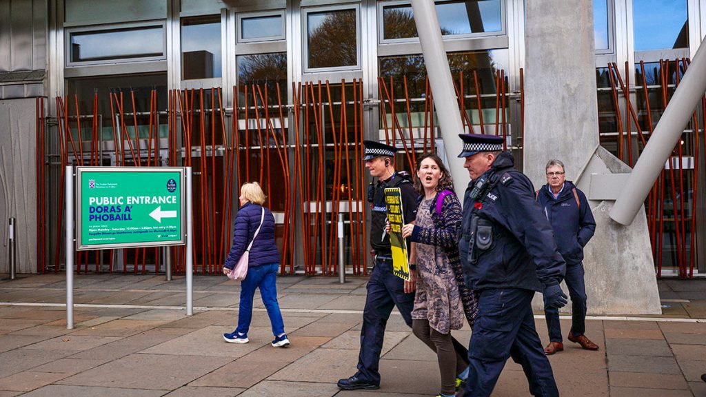 Arrested XR Scotland activist being led away by police outside Scottish Parliament during carbon capture is a scam protest.