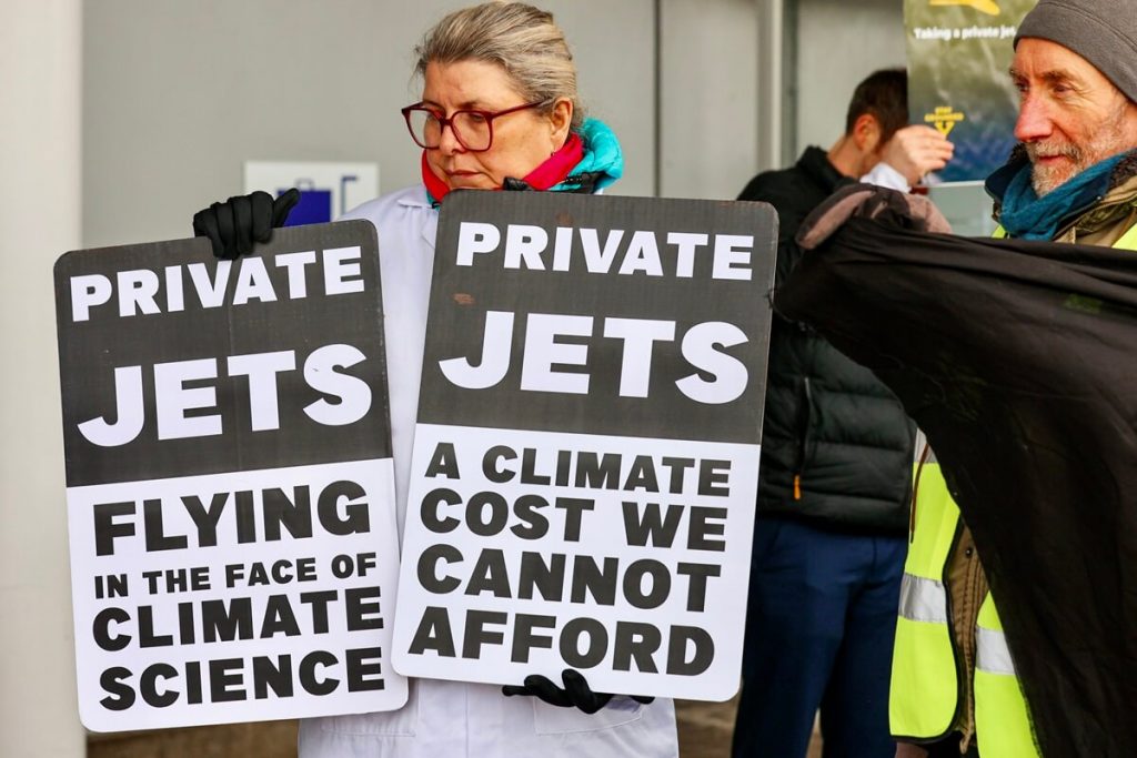 Protestors hold placards saying Private Jets - Flying in the Face of Climate Science and Private Jets - A climate costs we cannot afford