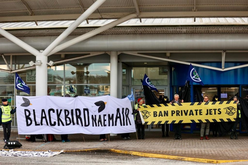 Protestors hold banners outside airport saying Blackbird Nae Mair and Ban Private Jets